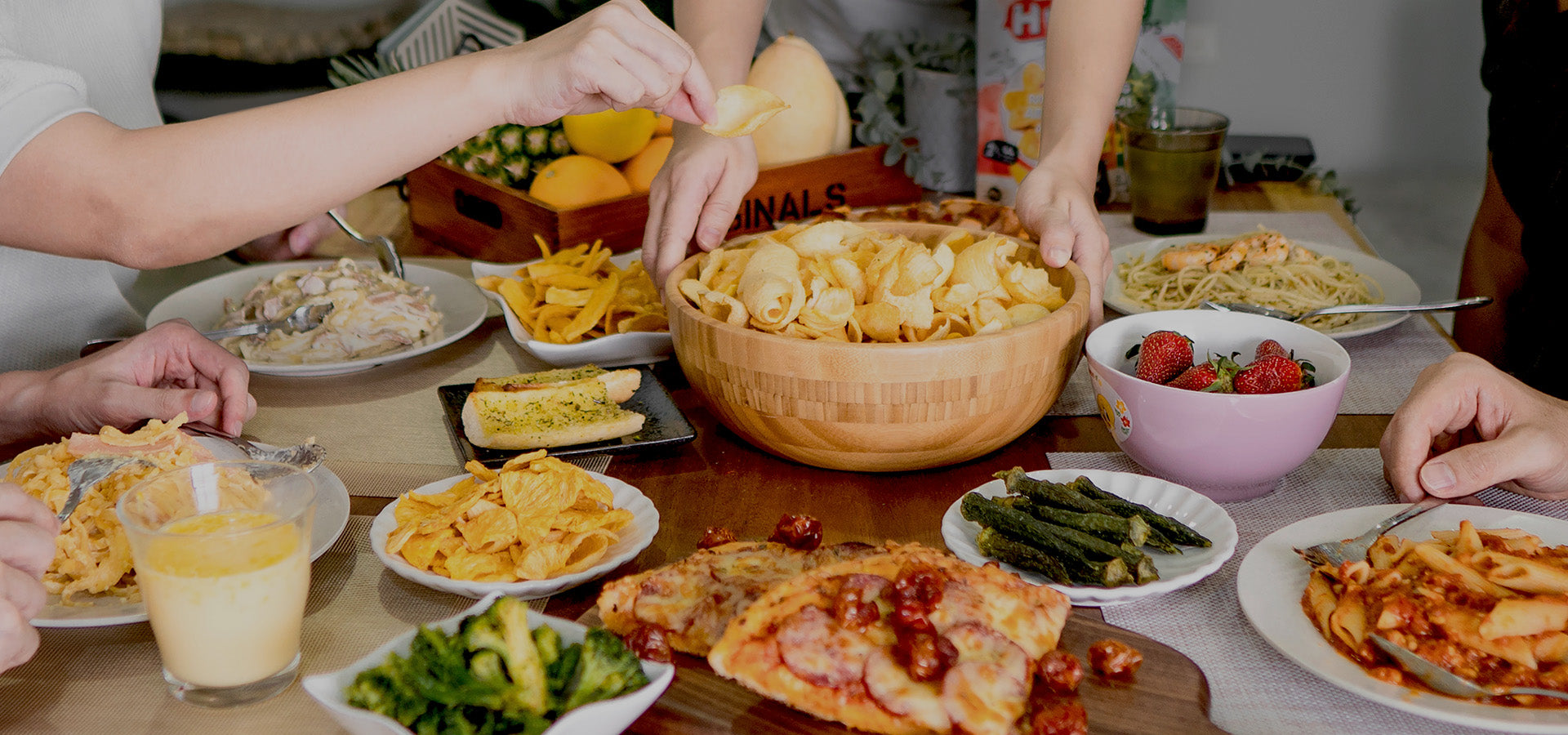 Table with various foods including pasta, pizza, and Hey! Chips okra and mango crisps.