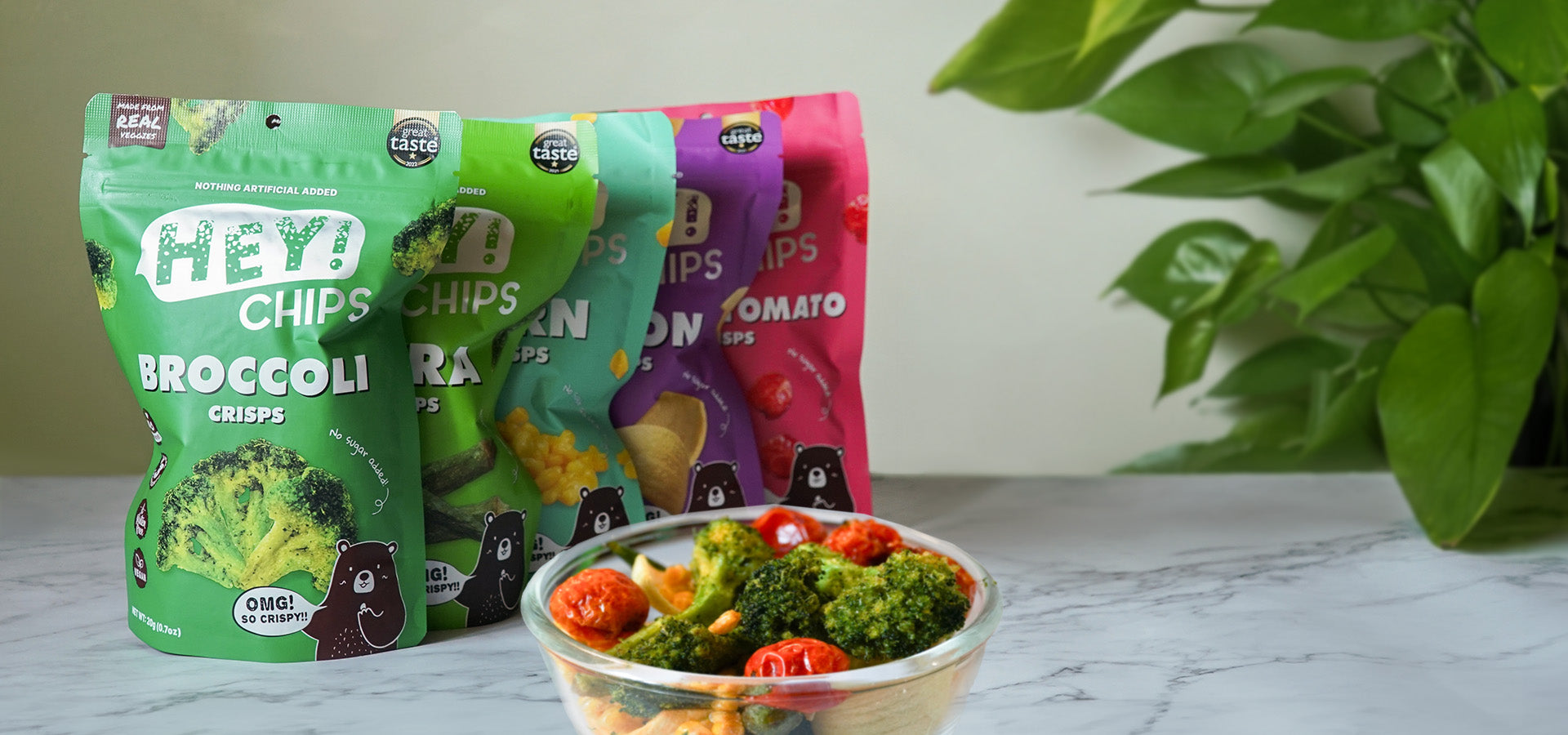 Hey! Chips products including broccoli, okra, corn, and more with actual crisps in a glass bowl on a table.