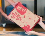 Hands passing a box of Hey! Chips.