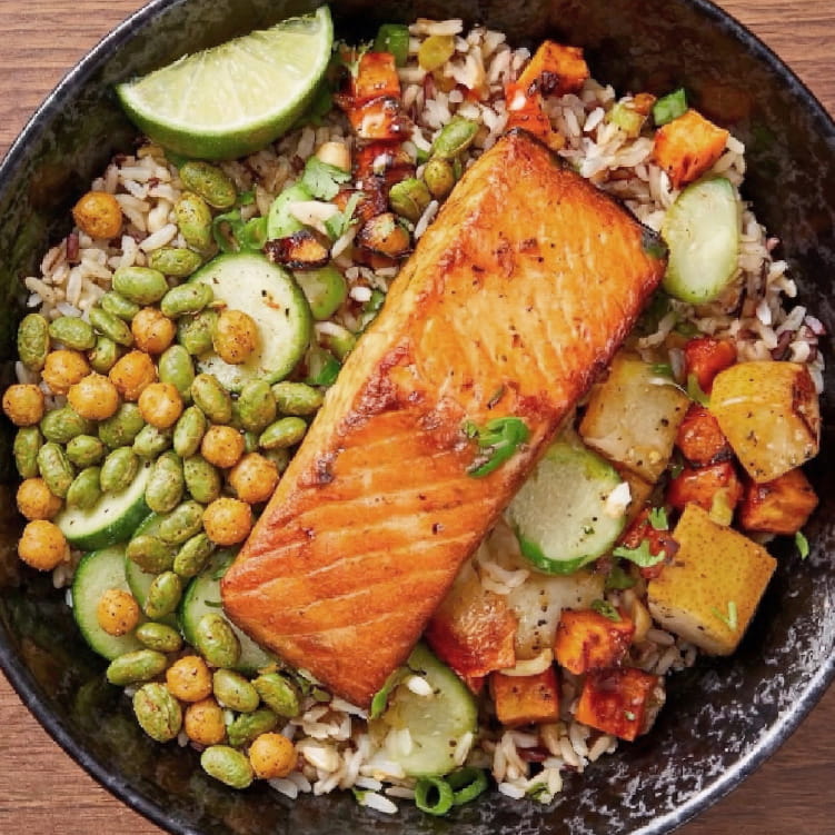 Salmon dish with rice, vegetables, lime wedges, and Superbeans on a wooden surface